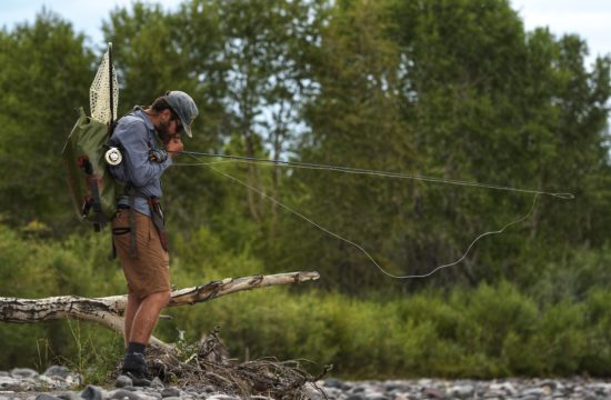 A fly fishing guide stands on the bank of a river with his fishing pole under his arm near CM Ranch in Dubois, WY | Wyoming dude ranch vacations