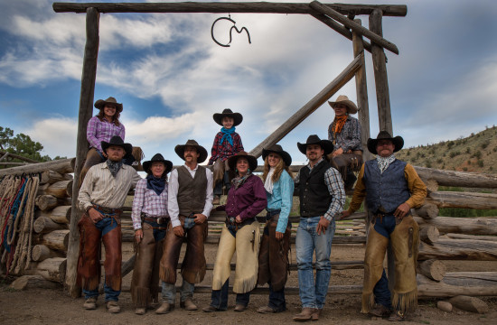 A group of adults and kids wearing leather hats, cowboy hats and boots pose for a photo under the CM Ranch sign in Dubois, WY | Wyoming dude ranch