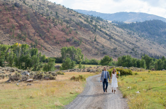 A newlywed couple walks hand in hand on a dirt road after their wedding ceremony at CM Ranch in Dubois WY | dude ranch Jackson Hoe